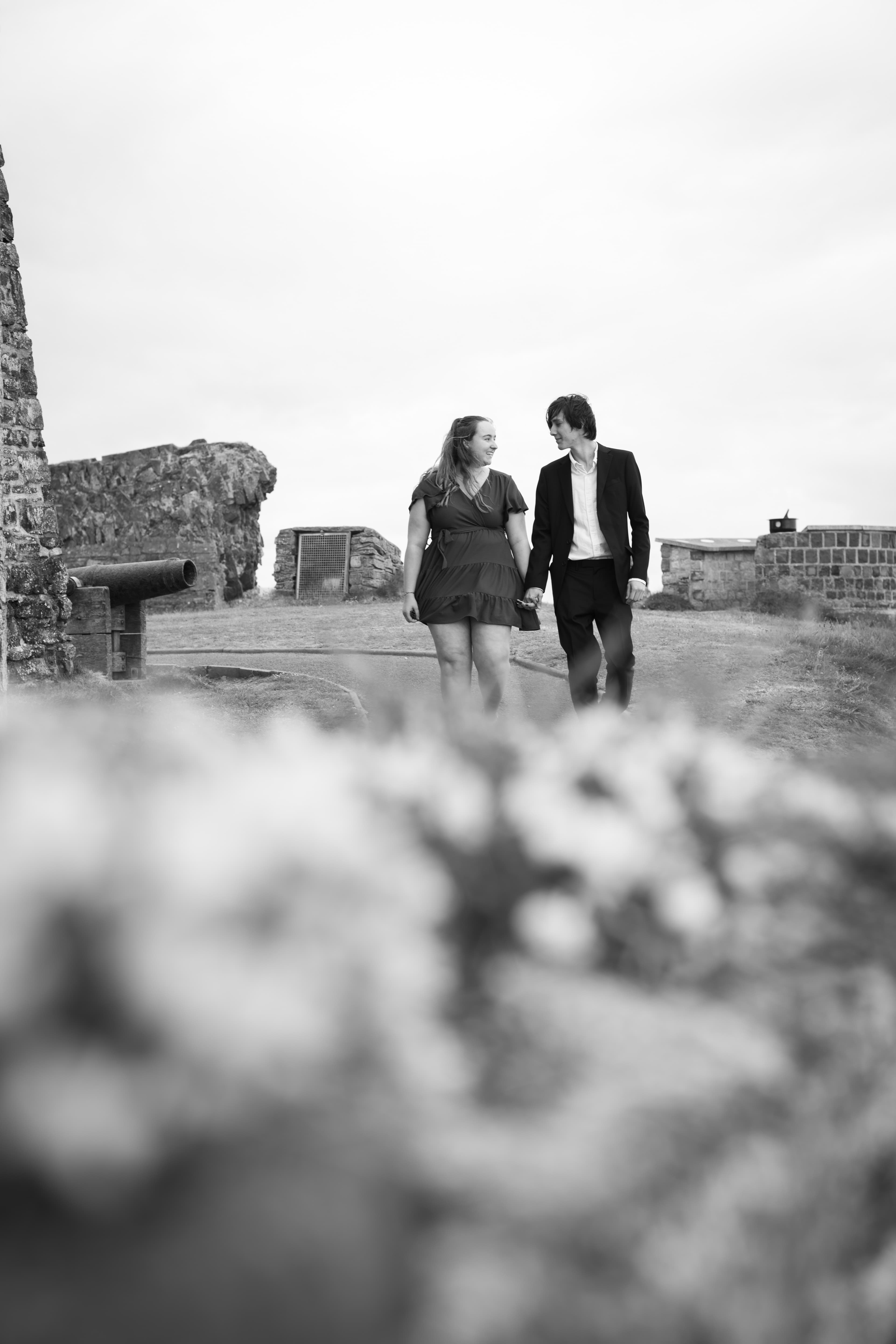 Hannah and Bradley walking hand in hand through castle ruins, in black and white